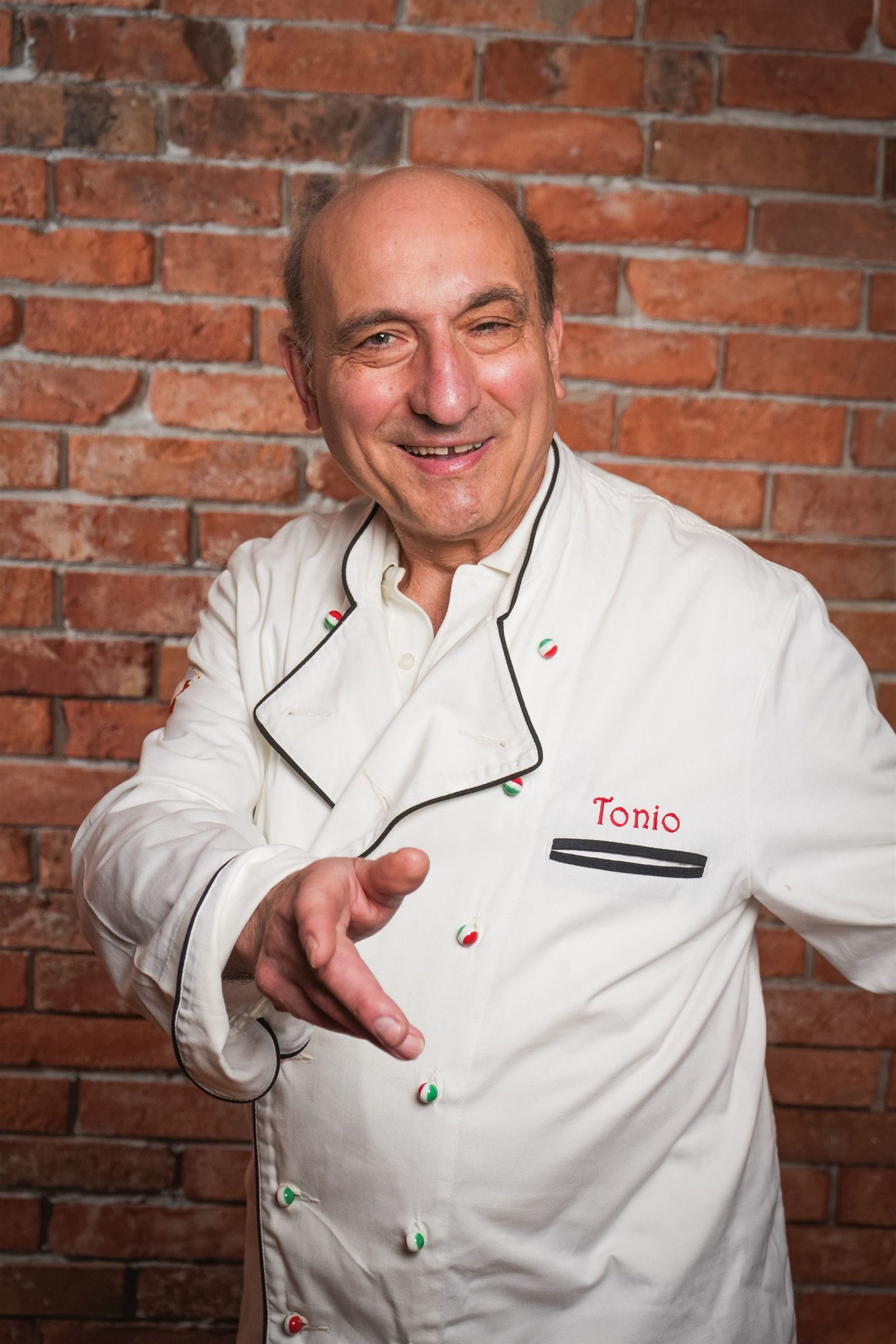 Maître Tonio Abbruzzi in seiner Kochjacke vor einer Backsteinwand